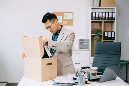 Téléchargez les photos : Asiatique employé de bureau prenant des choses personnelles tout en quittant le travail dans un bureau moderne, changer ou entreprise - en image libre de droit
