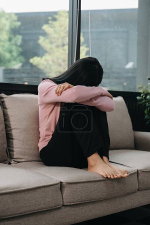 Foto de Mujer asiática sintiendo depresión sentada en el sofá de la casa - Imagen libre de derechos