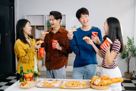 Foto de Grupo de jóvenes amigos asiáticos teniendo, disfrutar de la fiesta nocturna juntos en casa. Atractivos hombres y mujeres jóvenes divirtiéndose, comiendo y disfrutando de bebidas, celebrando en el hogar moderno - Imagen libre de derechos