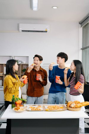 Téléchargez les photos : Groupe de jeunes amis asiatiques ayant, profiter de soirée ensemble à la maison. Jeunes hommes et femmes attrayants qui s'amusent, mangent et boivent, fêtent chez eux - en image libre de droit