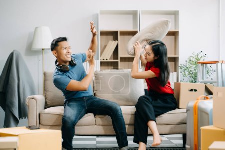 Téléchargez les photos : Jeune couple avec de grandes boîtes emménageant dans une nouvelle maison se battant avec les oreillers - en image libre de droit