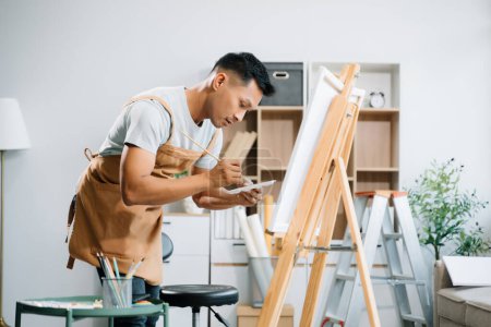 Téléchargez les photos : Peintre asiatique faisant des œuvres d'art dans un atelier d'art, fournitures de peinture, pastels à l'huile, chevalet en toile, espace créatif dans un atelier d'art - en image libre de droit