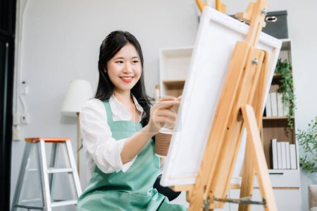 Téléchargez les photos : Asiatique peintre femme faisant des œuvres d'art dans l'atelier d'art, en utilisant des fournitures de peinture, pastels à l'huile, espace créatif dans l'atelier d'art - en image libre de droit