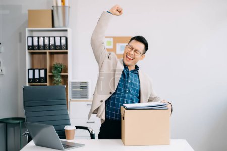 Téléchargez les photos : Joyeux et excité jeune travailleur de bureau asiatique célébrant sa démission tout en quittant son emploi dans un bureau moderne, un changement ou une entreprise - en image libre de droit