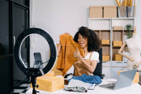 Téléchargez les photos : Concept de blogueur de mode, Jeune femme vendant des vêtements en streaming vidéo par smartphone. Création de petites entreprises PME - en image libre de droit