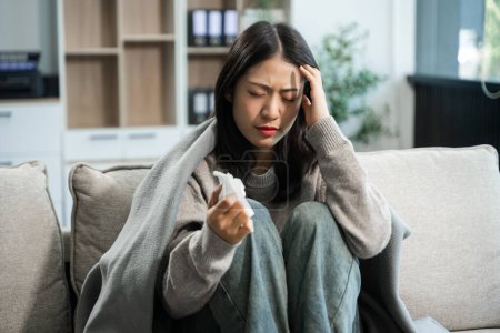 Mujer asiática joven que sufre de síntomas de gripe, cubierta con una manta en un sofá. Concepto de enfermedad, salud y recuperación