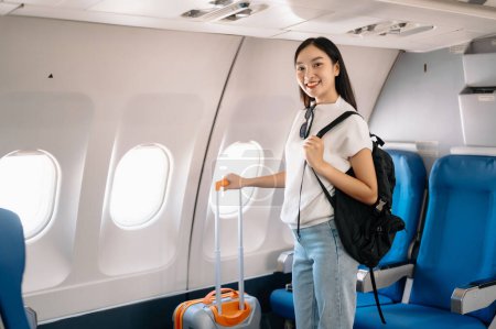 Foto de Atractiva mujer asiática pasajera de avión de pie en el salón con maleta y mochila. Estilo de viaje - Imagen libre de derechos