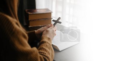 Foto de Mujer sentada y estudiando las escrituras. La cruz de madera en las manos. Conceptos de educación cristiana Las Sagradas Escrituras se abren y rezan a Dios - Imagen libre de derechos