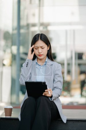 Asian businesswoman is stressed, bored, and overthinking from working with tablet pc and coffee