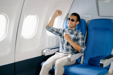 Happy Asian man sitting in a seat in airplane and having cup of coffee, going on a trip. 