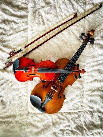 Deux tailles différentes de violons et d'arcs mis sur tissu de coton doux, montrent le détail de l'instrument acoustique.