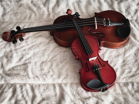 Dos tamaños diferentes de violines se ponen en tela de algodón suave, muestran el detalle del instrumento acústico.