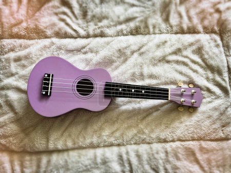 Ukulele made from wood  in purple color put on soft cloth background,Hawaiian acoustic instrument,blurry light around