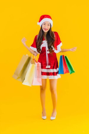 Foto de Retrato hermosa joven asiática mujer usar navidad ropa sombrero con un montón de bolsa de compras en amarillo aislado fondo - Imagen libre de derechos