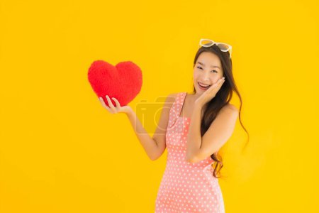 Photo for Portrait beautiful young asian woman with heart pillow sign on yellow isolated background - Royalty Free Image