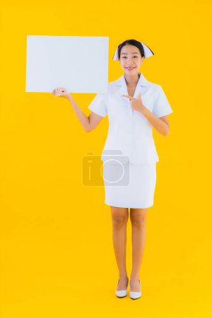 Photo for Portrait beautiful young asian woman thai nurse show empty white board and work at clinic or hospital on yellow isolated background - Royalty Free Image