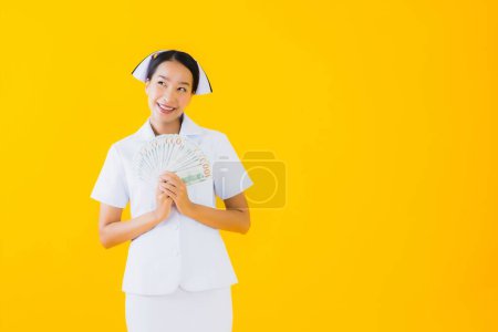 Photo for Portrait beautiful young asian woman thai nurse with a lot of cash and money and pink piggy bank on yellow isolated background - Royalty Free Image