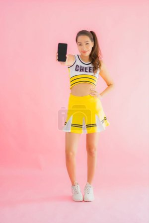 Téléchargez les photos : Portrait belle jeune femme asiatique pom-pom girl avec téléphone portable intelligent sur fond rose isolé - en image libre de droit