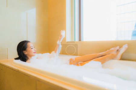 Foto de Retrato hermosa joven asiática mujer relajarse sonrisa ocio en bañera en baño interior - Imagen libre de derechos