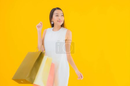 Téléchargez les photos : Portrait belle jeune femme asiatique avec sac à provisions de détaillants grand magasin sur fond jaune isolé - en image libre de droit
