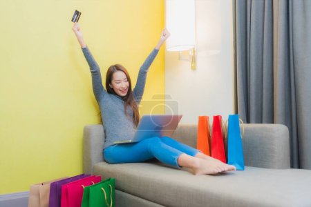 Téléchargez les photos : Portrait belle jeune femme asiatique utiliser ordinateur portable avec carte de crédit pour les achats en ligne sur canapé dans le salon - en image libre de droit
