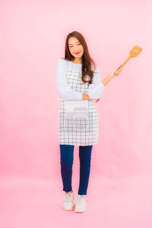 Téléchargez les photos : Portrait belle jeune femme asiatique en tenue de cuisine avec tablier sur fond rose isolé - en image libre de droit