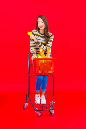 Foto de Retrato hermosa joven asiática mujer con cesta de supermercado en rojo aislado fondo - Imagen libre de derechos