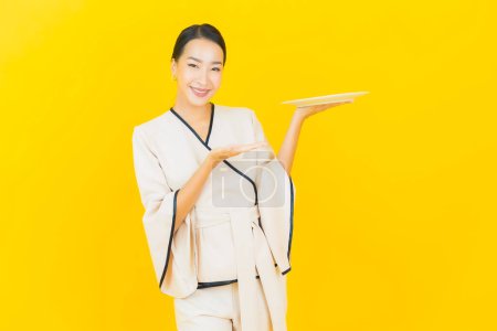 Téléchargez les photos : Portrait belle jeune femme asiatique d'affaires avec plaque de plat vide sur fond jaune - en image libre de droit