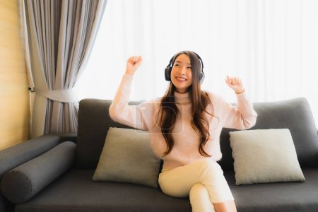 Photo for Portrait beautiful young asian woman using smart mobile cell phone  and headphone for listen music on sofa in living room interior - Royalty Free Image