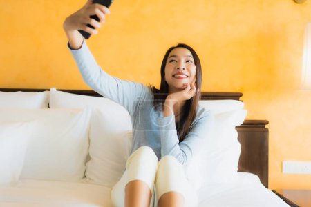 Téléchargez les photos : Portrait belle jeune femme asiatique en utilisant un téléphone portable sur le lit avec tasse de café à l'intérieur de la chambre - en image libre de droit