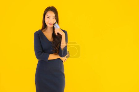 Foto de Retrato hermosa mujer asiática joven con teléfono móvil inteligente o teléfono celular y tarjeta de crédito amarillo aislado fondo - Imagen libre de derechos