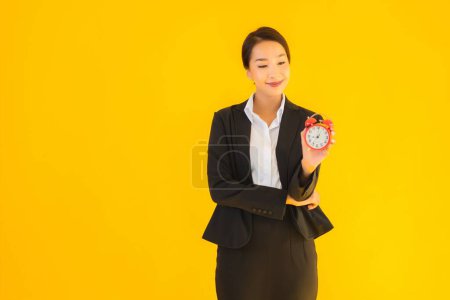 Photo for Portrait beautiful young asian woman show time of clock or alarm on yellow isolated background - Royalty Free Image
