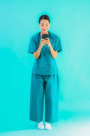 Foto de Retrato hermosa joven asiática médico mujer espectáculo inteligente teléfono móvil en azul aislado fondo - Imagen libre de derechos