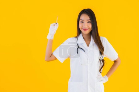 Téléchargez les photos : Portrait belle jeune asiatique médecin femme porter gant utilisation seringue sur jaune isolé fond - en image libre de droit