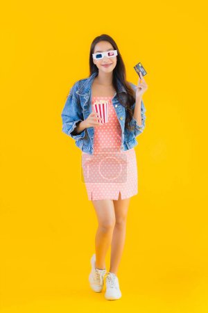 Photo for Portrait beautiful young asian woman ready to watch movie with popcorn and credit card on yellow isolated background - Royalty Free Image