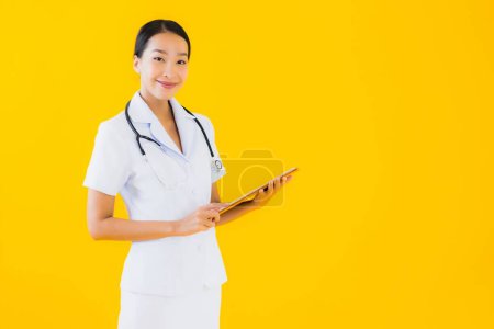 Foto de Retrato hermosa joven asiática mujer tailandesa enfermera sonrisa feliz listo para el trabajo para paciente en clínica u hospital en amarillo aislado fondo - Imagen libre de derechos