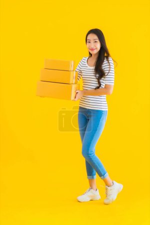 Téléchargez les photos : Portrait belle jeune femme asiatique avec boîte de colis prêt pour l'expédition sur fond jaune isolé - en image libre de droit