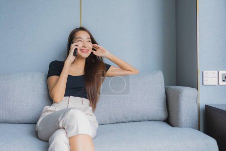 Téléchargez les photos : Portrait belle jeune femme asiatique utiliser téléphone portable intelligent sur canapé dans le salon - en image libre de droit
