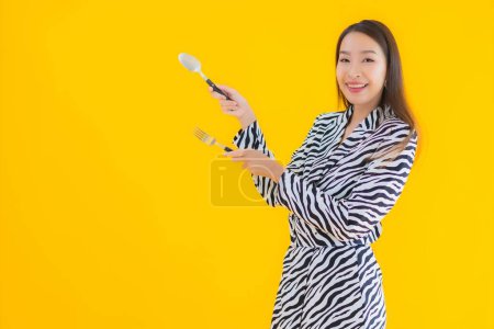 Foto de Retrato hermosa joven asiática mujer con cuchara y tenedor listo para comer en amarillo aislado fondo - Imagen libre de derechos