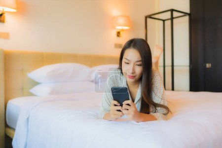 Foto de Retrato hermosa joven mujer asiática en la cama con teléfono móvil inteligente en el interior del dormitorio - Imagen libre de derechos
