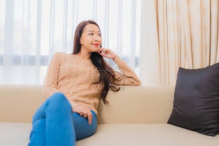 Foto de Retrato hermosa joven mujer asiática relajarse sonrisa feliz en sofá decoración interior del dormitorio - Imagen libre de derechos