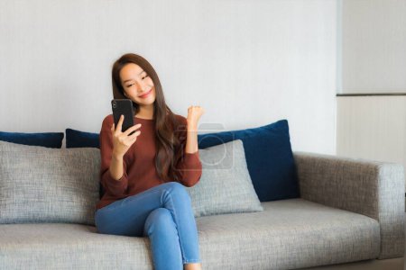 Foto de Retrato hermosa joven mujer asiática uso de teléfono inteligente en sofá en el interior de la sala de estar - Imagen libre de derechos