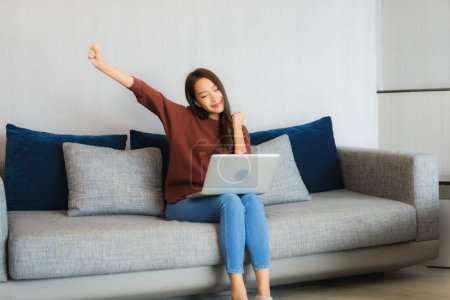 Téléchargez les photos : Portrait belle jeune femme asiatique utiliser ordinateur portable sur canapé dans le salon intérieur - en image libre de droit