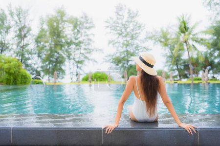 Foto de Retrato hermosa joven mujer asiática relajarse sonrisa ocio alrededor de la piscina al aire libre en el complejo hotelero casi playa de mar - Imagen libre de derechos