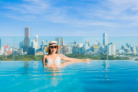 Foto de Retrato hermosa joven mujer asiática sonrisa relajarse ocio alrededor de piscina al aire libre con vista a la ciudad - Imagen libre de derechos