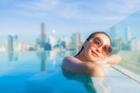 Téléchargez les photos : Portrait belle jeune femme asiatique sourire détendre loisirs autour de la piscine extérieure avec vue sur la ville - en image libre de droit