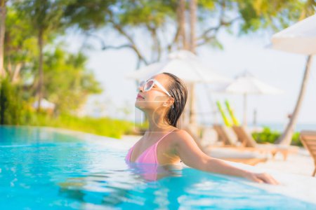 Téléchargez les photos : Portrait belle jeune femme asiatique se détendre loisirs autour de la piscine extérieure avec vue sur la mer plage océan en vacances Voyage - en image libre de droit