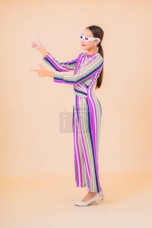 Téléchargez les photos : Portrait belle jeune femme asiatique porter des lunettes 3D pour regarder le film sur fond isolé couleur - en image libre de droit