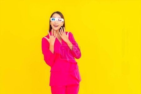 Téléchargez les photos : Portrait belle jeune femme asiatique porter des lunettes 3d pour regarder un film sur fond jaune isolé - en image libre de droit