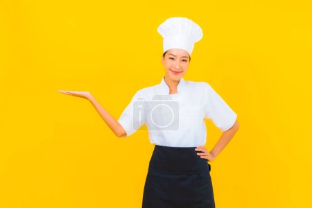 Foto de Retrato hermosa joven asiática mujer en chef o cocinero uniforme con sombrero en amarillo aislado fondo - Imagen libre de derechos